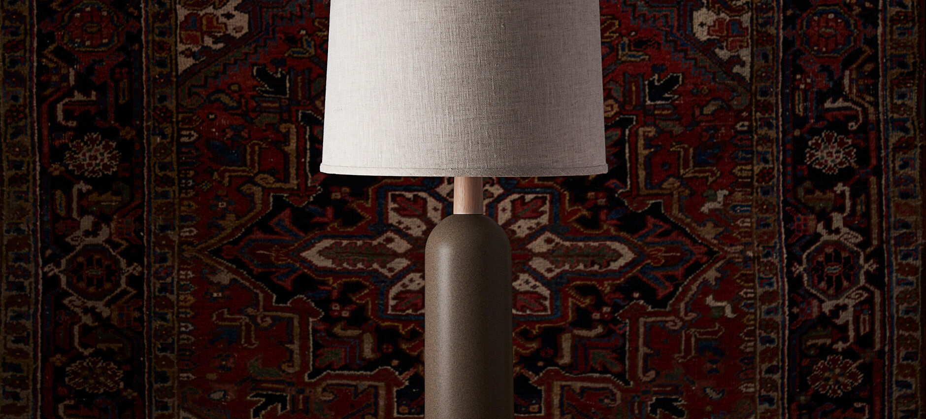 Modern ceramic table lamp with a linen shade displayed against a richly patterned vintage rug backdrop.